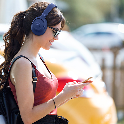 Слушалки JBL Tune 780NC, сини, носени в града, с телефон в ръка