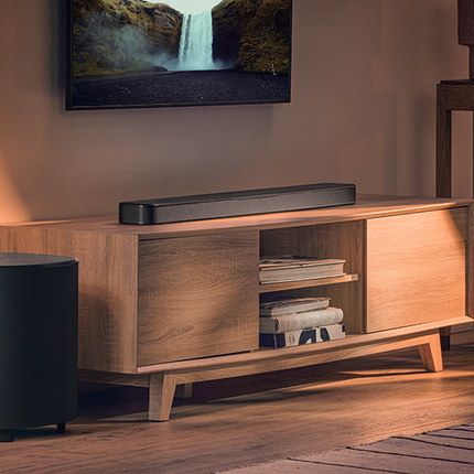 JBL Bar 500MK2 върху шкаф със субуфера до него, под телевизор на стената