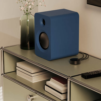 Kanto Audio REN в син цвят на скрин, до дистанционното и книги