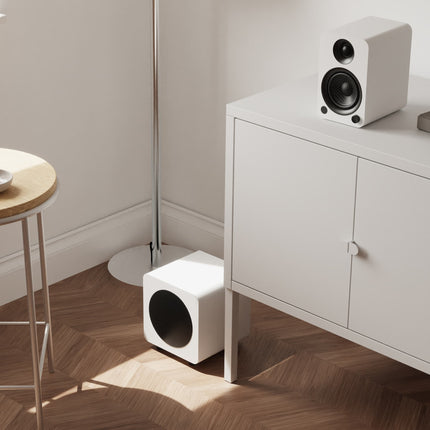 Субуфер Kanto Audio SUB6, матово бяло, на пода в обзаведена стая, близо до тонколони
