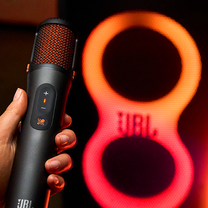 Микрофон JBL EasySing Mics в ръка пред светлините на тонколона JBL PartyBox